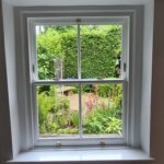 New white sliding sash window by Patchett Joinery with a view into a garden.