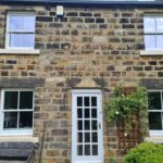 Old yellow stone house in Leeds with four new white sliding sash windows and a White timber door with sections
